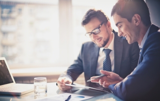 Image of two young businessmen using touchpad at meeting